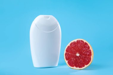 Canlı mavi arka planda taze greyfurtun yanında beyaz bir şişenin görüntüsü, tazelik ve temizlik, cilt bakımı veya sağlık ürünleri temaları için ideal.