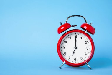 Geleneksel bir kırmızı alarm saati yumuşak mavi arka planda gösterilir. Saat, zaman yönetimi ve aciliyeti sembolize ederek saat 12 'deki kilidi gösteriyor..