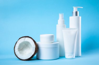 Canlı mavi arka planda taze hindistan cevizi sergilenen çeşitli beyaz tenli şişeler. Tazelik ve saflığı vurgulayan güzellik, sağlık ve cilt ürünleri için idealdir..