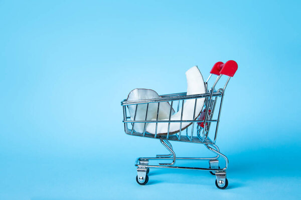 Creative concept of coconut slices in a miniature shopping cart against a bright blue background, symbolising fresh grocery shopping and tropical vibes.