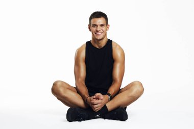 Tutkulu genç erkek bir stüdyoda bacak bacak üstüne atmış, atletik enerji yayıyor ve beyaz arka planda izole edilmiş pozitif bir tutum sergiliyor. Fitness markalaşma ve yaşam tarzı promosyonları için ideal.