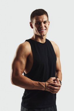 Siyah kolsuz tişörtlü kaslı bir gencin dikey portresi kendine güvenen ve arkadaş canlısı bir ifade sergiliyor, aktif ve sağlıklı bir yaşam tarzını sembolize ediyor..