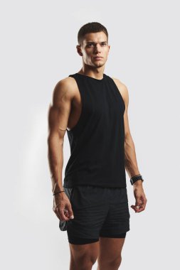 Modern bir stüdyo ortamında siyah spor kıyafetleri giyen kaslı bir erkek. Sportif görünüş, güç, adanmışlık ve stili vurgular, tarafsız renkli bir arkaplanda yakalanır.