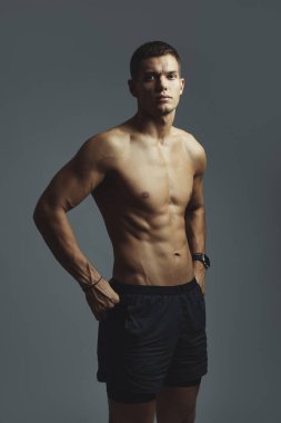 Formda ve kendinden emin genç bir adam atletik siyah şortuyla poz verirken kaslı ve kaslı vücudunu gösterir. Kaslı adam atletizmi ve sağlık ve zindeliğe bağlılığı vurguluyor.