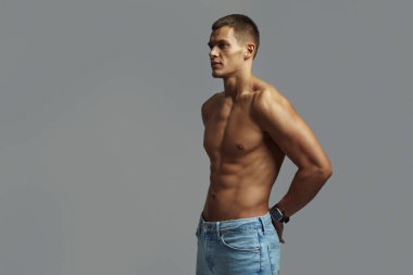 Kot pantolon giyen ve gri arka planda poz veren formasız genç bir adam. Öznelerin varlığını arttırmak için minimalist bir zemin ile güç, zindelik ve özgüven vurgulanıyor.