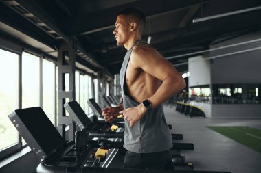 Modern spor salonunda koşu bandında koşan bir sporcunun yan görüntüsü. Spor kulübünde sağlık ve spor üzerine çalışmak. Sağlıklı bir yaşam tarzı, spor salonunda antrenman yapan bir adam. Spor çalıştırma konsepti.