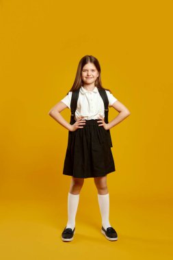 Neşeli genç öğrenci, elleri kalçasında gururla duruyor, okula hazır olduğunu ve özgüvenini gösteriyor. Eğitici tanıtım materyalleri ve reklamlar için mükemmel..