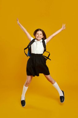 Mutlu çocuk enerjik bir şekilde okul kıyafetiyle atlıyor, heyecan ve neşe sergiliyor. Eğitim promosyonları ve okul kampanyaları için ideal..