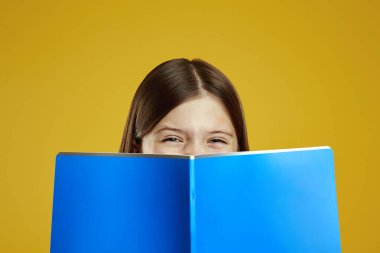 Parlak gözlü neşeli bir çocuk canlı mavi bir defterin üzerinde gülümsüyor, neşeli ve meraklı bir ruh hali yaratıyor. Eğitim içeriği veya okul reklamları için ideal.