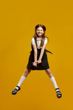 Enerjik bir çocuk, klasik okul kıyafetleri içinde, neşeli bir gülümseme ve coşkuyla havalara uçuyor. Eğitici promosyonlar ve oyuncu reklamlar için ideal..