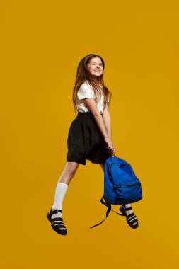 Neşeli genç enerjik bir şekilde parlak mavi bir sırt çantasıyla atlıyor, canlı sarı bir arka plana mutluluk saçıyor. Okul temalı promosyonlar ve reklamlar için harika..