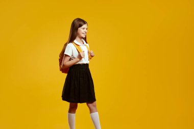 Sırt çantası takan mutlu bir çocuk, parlak sarı bir arkaplanda güvenle yürüyor, coşku ve hazırlık hissi uyandırıyor. Eğitim promosyonları ve okul kampanyaları için ideal.