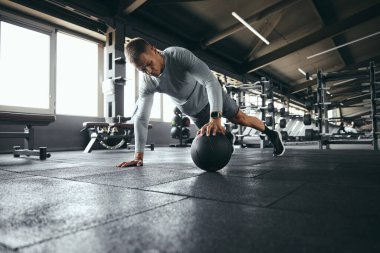 Spor kıyafetli güçlü bir adamın, modern spor salonunda yoğun spor yaparken tek eliyle şınav çekerken çekilmiş yatay fotoğrafı.