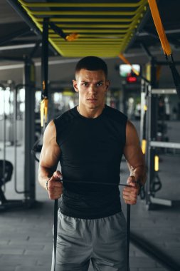 Spor kıyafetlerindeki güçlü yakışıklı adam spor salonunda dayanıklılık ve kas gelişimini vurgulayarak elastik direnç bandıyla tüm vücudunu çalıştırıyor..