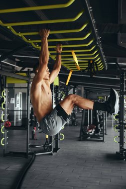 Modern spor salonundaki barda karın kası egzersizi yapan kaslı, güçlü bir adamın dikey fotoğrafı.