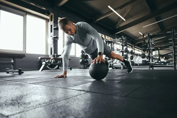 Spor kıyafetli güçlü bir adamın, modern spor salonunda yoğun spor yaparken tek eliyle şınav çekerken çekilmiş yatay fotoğrafı.