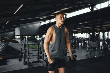 Spor giyim bölümündeki formda vücut geliştiren adam modern spor salonunda halterli kasları çalıştırıyor. Vücut geliştirme, fitness ve sağlık hizmeti kavramı.