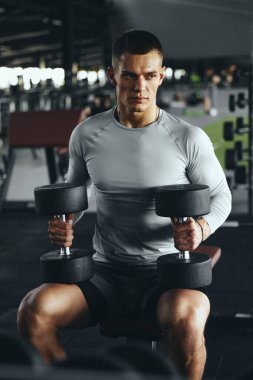 Spor bankında dambılla egzersiz yapan güçlü bir adam. Güç eğitimi, disiplin ve iş başındaki yaşam tarzı.