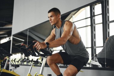 Modern spor salonunda spor kıyafetleri içinde bisiklete binen formda bir genç. Spor ve sağlık hizmetleri kavramı.