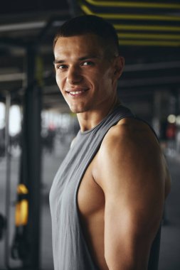 Spor salonundan sonra sporcu bir sporcunun dikey portresi. Spor kıyafetleriyle yakışıklı bir fitness hocasının yatay fotoğrafı. Kameraya poz verirken gülümsüyor..