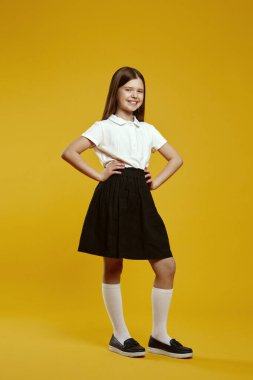Neşeli bir çocuk, parlak, renkli bir arkaplan karşısında klasik bir okul üniforması içinde, mutluluk ve pozitifliği ifade ederek güven içinde poz verir. Eğitici pazarlama materyalleri için ideal.