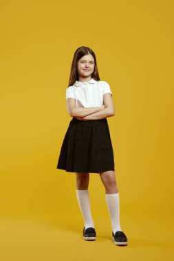 Neşeli bir çocuk, elleri klasik bir okul üniforması içinde parlak sarı bir arka planda güvenle duruyor. Eğitim terfileri ve okul kampanyaları için ideal.