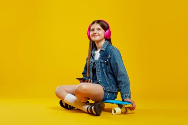 Kot ceket giyen, kulaklıkla müzik dinleyen, akıllı telefon tutan ve kaykayın üzerinde otururken yüzünü çeviren neşeli bir çocuk. Gençlik yaşam tarzı ya da müzik temalı promosyonlar için ideal