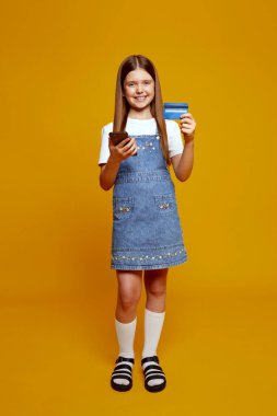 Kot elbiseli neşeli çocuk elinde akıllı telefon ve kredi kartı ile modern dijital yaşam tarzını sembolize ediyor. Çevrimiçi hizmetlerde reklam ve eğitim içeriği için ideal.