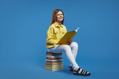 Gülümseyen gözlüklü ve sarı ceketli genç kitap okurken mutluluk ve merak saçmaktan zevk alıyor. Eğitime veya öğrenmeye odaklı içerik için ideal.