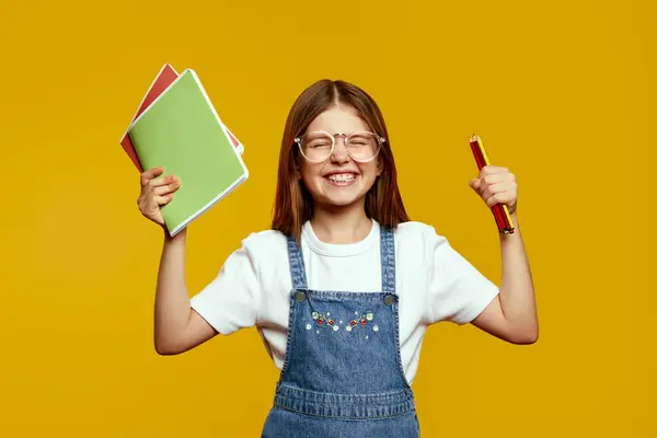 Renkli defterler ve kalemlerle dolu gözlüklü neşeli bir çocuk canlı bir arkaplanda heyecan ve neşe ifade ediyor. Eğitimsel promosyonlar ve okul materyalleri için ideal.