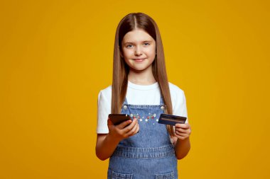 Akıllı telefon ve kredi kartı tutan neşeli çocuk modern dijital yaşam tarzını sergiliyor. Çocuklar için finansal okur-yazarlık konusunda eğitici içerik için ideal.