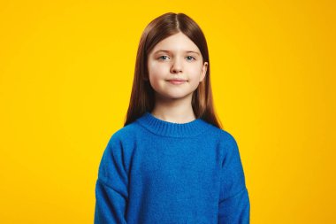 Samimi mavi süveterli masum bir çocuk, sakin bir şekilde sarı bir arkaplanda poz veriyor. Huzur ve sıcaklık hissi veriyor..