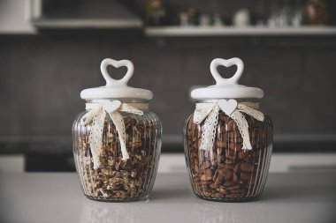 Karışık fındıkla dolu, dantel ve kalp şeklinde kapaklarla süslenmiş iki kırsal cam kavanoz davetkar ve rahat bir mutfak atmosferi yaratıyor..