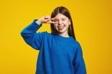 Neşeli çocuk, cesur sarı bir zemine kurulmuş, barış işareti ve küstah bir ifadeyle oyunculuğunu ifade ediyor. Neşeli promosyonlar ya da çocuk içeriği için ideal.