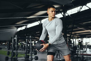 Spor salonunda ağırlık topuyla egzersiz yapan bir gencin yatay görüntüsü var. Güçlü, atletik figür fiziksel dayanıklılık ve bağlılık gösteriyor.