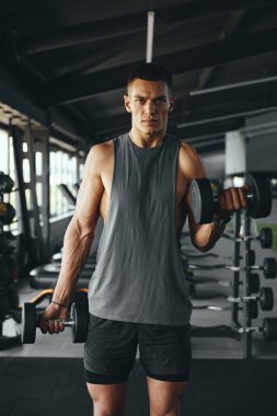 Modern spor salonunda ağırlık kaldıran çekici vücut geliştiren adamın dikey fotoğrafı. Vücut geliştirme, fitness ve sağlık hizmeti kavramı.