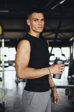 Spor salonundaki güçlü ve odaklanmış erkek sporcu ciddi ifadeli bir spor sallayıcısı tutuyor. Disiplini, fitness zihniyetini ve kişisel sağlık hedeflerine olan bağlılığını yansıtıyor..