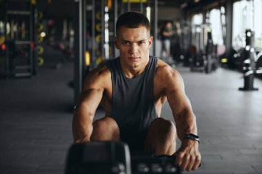 Çağdaş jimnastik salonunda kürek çeken konsantre çekici bir adam. Spor salonunda kürek çekme konusunda aktif bir genç adam eğitimi. Ağırlık azaltma ve kardiyovasküler fitness fikri.