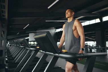 Hareketli giyinen atletik bir adam modern bir spor salonundaki koşu bandına odaklandı. Koşu pistinde çok çekici bir erkek ısınıyor. Sağlıklı bir yaşam tarzı, spor salonunda antrenman yapan bir adam. Spor çalıştırma konsepti.