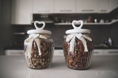 Kalp şeklinde kapaklı cam kavanozlar ve dantel kurdeleler ceviz ve badem tutuyor. Mutfak dekorasyonu, depolama ve hediye için mükemmel. Modern mutfak düzeni biraz zarafet katıyor..
