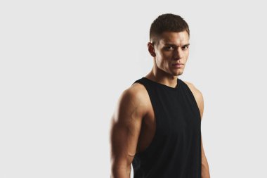 Siyah kolsuz bluz giyen odaklanmış sporcu açık gri arka plan, fiziksel zindelik ve motivasyon ruhuna karşı kararlılıkla poz veriyor. Vücut geliştirme, fitness ve sağlık konsepti