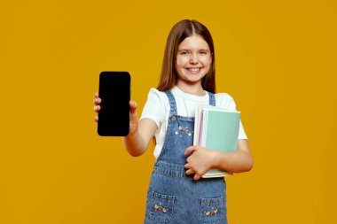 Neşeli çocuk okul kitaplarını tutarken akıllı telefon sergiliyor, neşe ve merak saçıyor. Eğitimsel promosyonlar ve teknolojiyle ilgili reklamlar için ideal.
