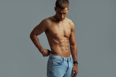 Güçlü ve atletik bireysel, zayıf ve formda, kot pantolon giyiyor, gri arka planda izole edilmiş.