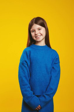 Neşeli genç rahat mavi bir kazak giyiyor, canlı sarı bir arka planda neşeli bir gülümseme ile kendine güvenerek duruyor. Çocuklar için mükemmel moda reklamları ve neşeli pazarlama malzemeleri.