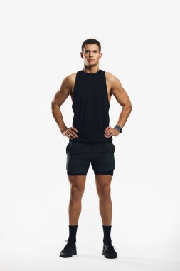 Aktif ve formda, siyah spor giysileri giyen genç adam, beyaz, parlak bir arka planda profesyonel bir stüdyoda kendine güvenen, güç ve kararlılık gösteren biri..