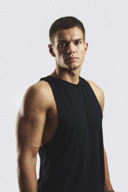 Siyah atletik gömlek giyen genç ve kaslı bir adam. Profil, güç, odak ve kararlılığı, zindelik, sağlık ve motivasyon kavramları için uygun gri bir arka plana karşı vurgular.