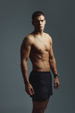 Kaslı üstsüz bir adamın dikey fotoğrafı ve portresi ya da stüdyo gururu, karın kasları ve forma mavi arka planda. Erkek, kendinden emin ve güçlü, karın kaslı.