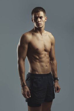 Atletik ve kaslı bir adam stüdyo ortamında kendinden emin bir şekilde dururken kaslı vücudunu sergiliyor. Fitness, sağlık, güç ve idmanla ilgili konular için ideal temsil.