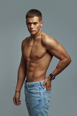 Formda ve kaslı bir adamın dikey fotoğrafı üstünkörü bir kot pantolonun içinde kendine güven ve zindelik gösteriyor. Sağlık, zindelik ve kendine güvenen bir yaşam tarzı için ideal..