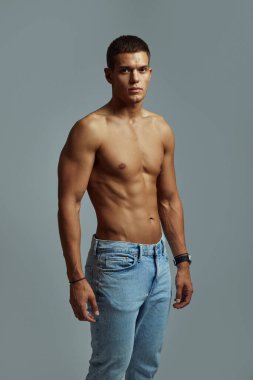 Formda, atletik fiziği olan yakışıklı genç adam kot pantolon içinde üstsüz poz veriyor. Onun tanımlanmış karın kasları, güçlü yapısı ve kendine güveni bu görüntüyü uygunluk, moda ve yaşam tarzı kavramları için ideal kılıyor..